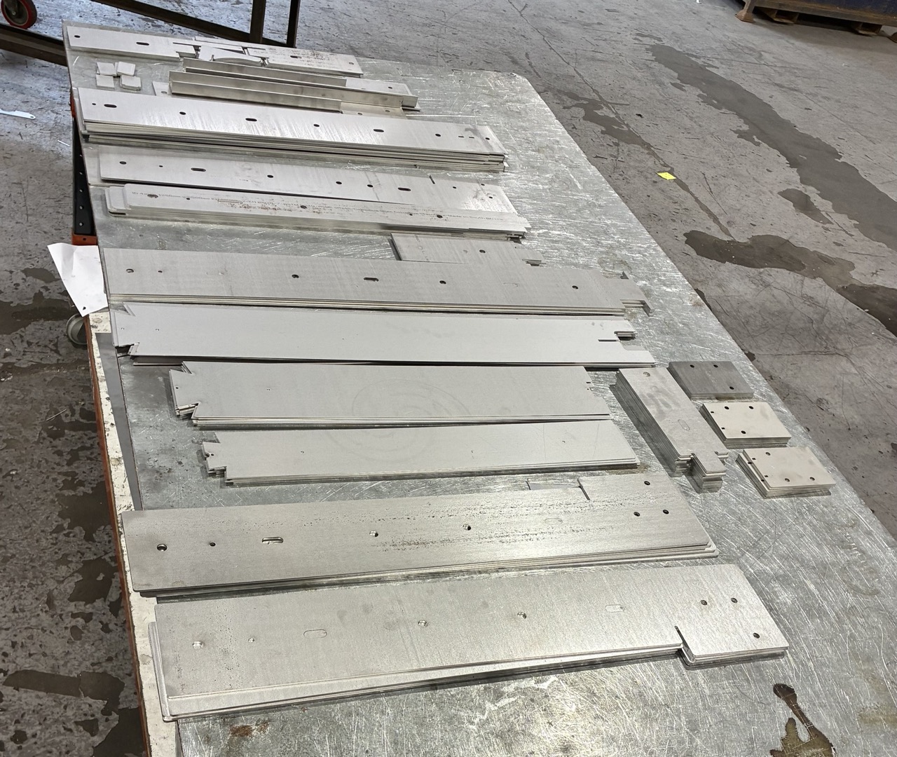 Stainless steel bracket components laid out on a galvanised table next to the press brake