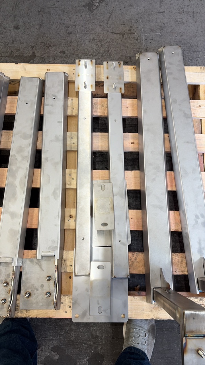 Range of bespoke LoadBear stainless brackets — pipe brackets, gutter brackets and spreader plates laid out on a pallet